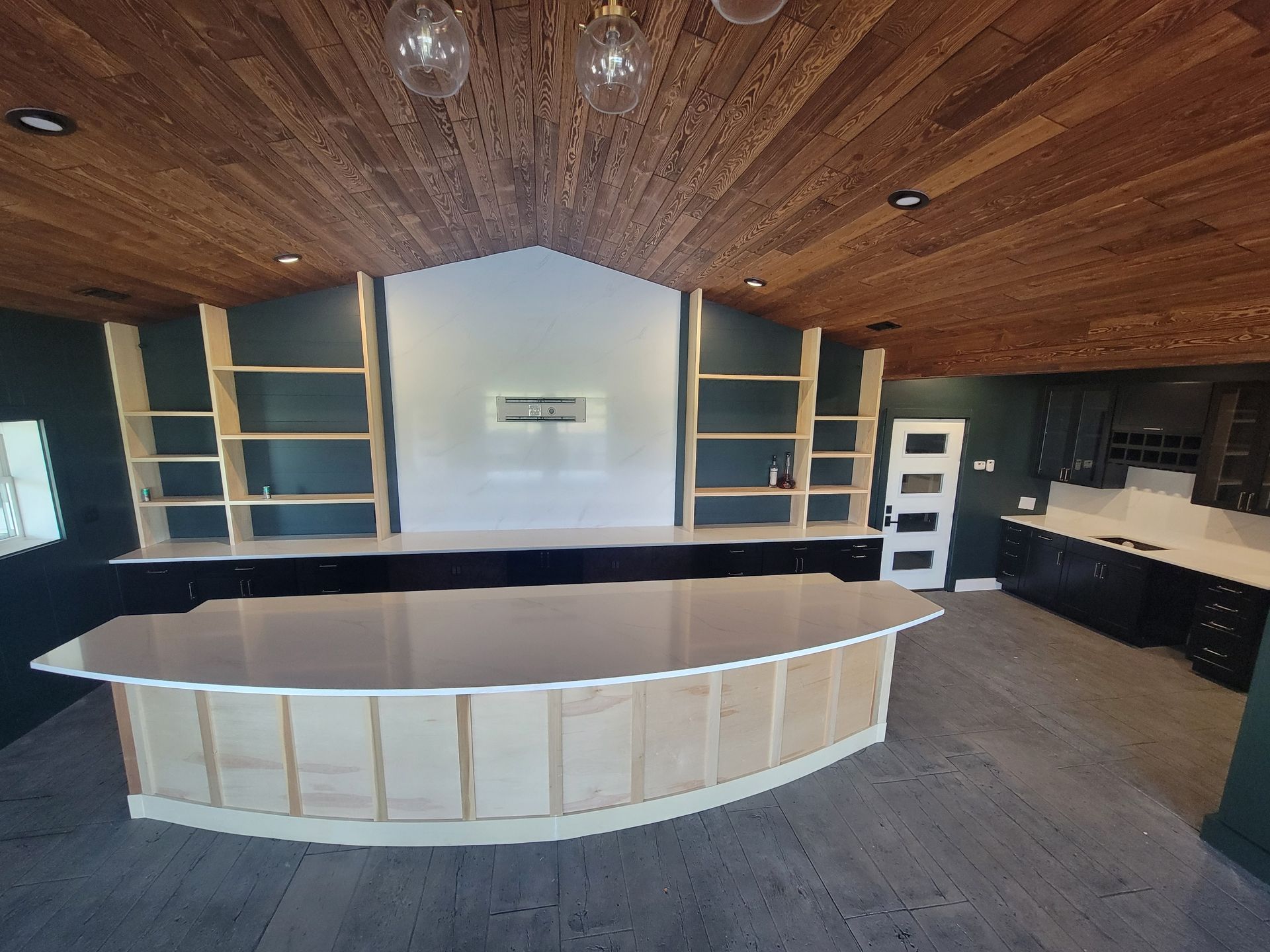 Empty modern kitchen with wood ceiling, black countertops, and a large curved white island
