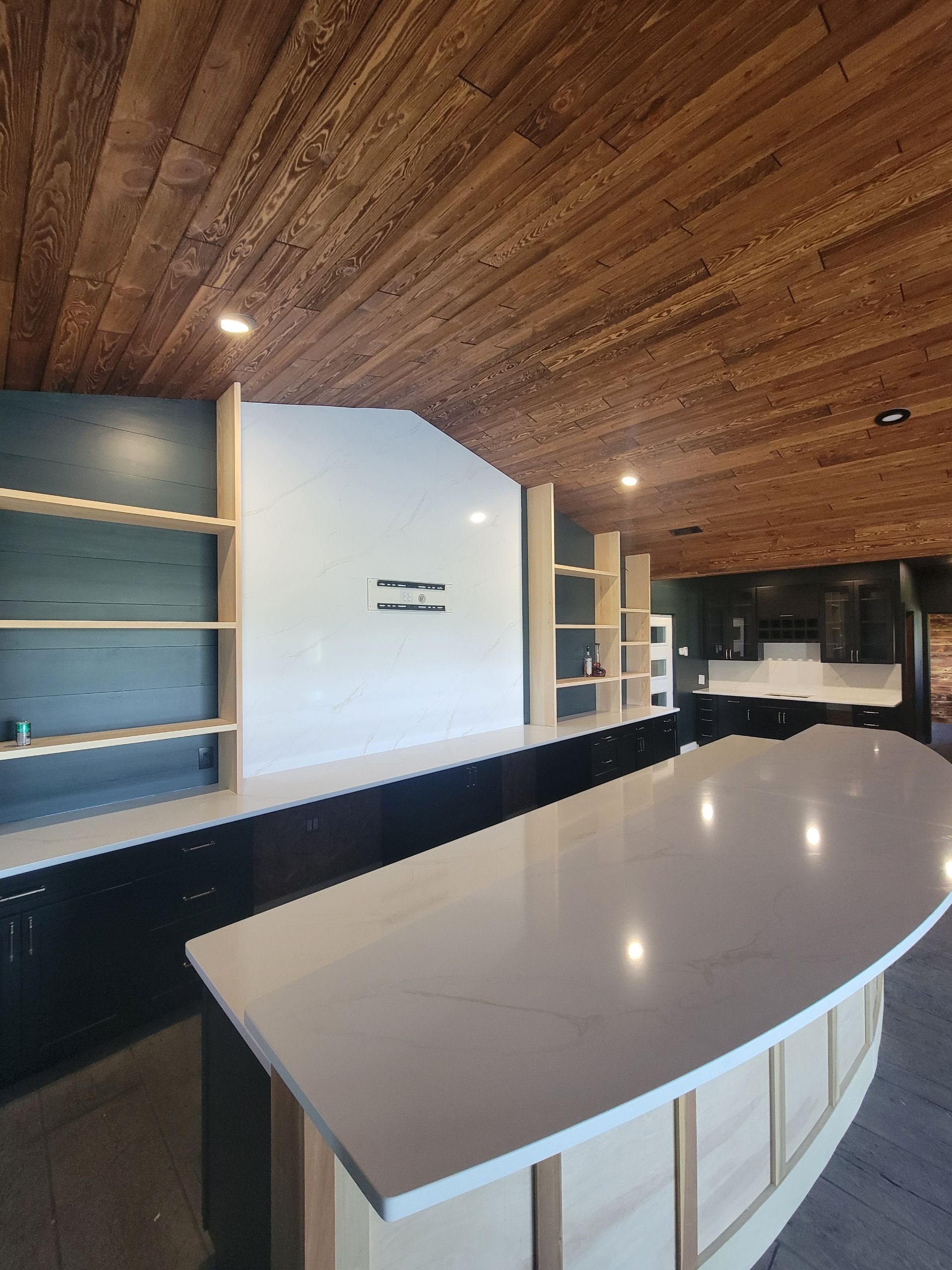 Empty modern kitchen with white island, wood ceiling, dark cabinets, and built-in shelves
