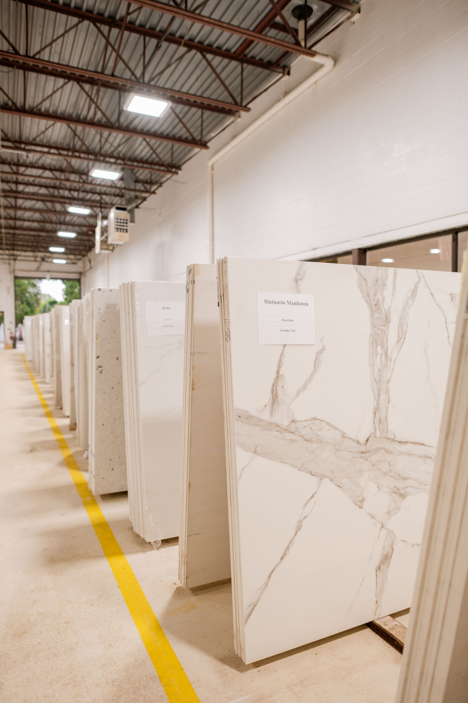 Rows of marble slabs displayed in an indoor warehouse aisle with yellow floor markings
