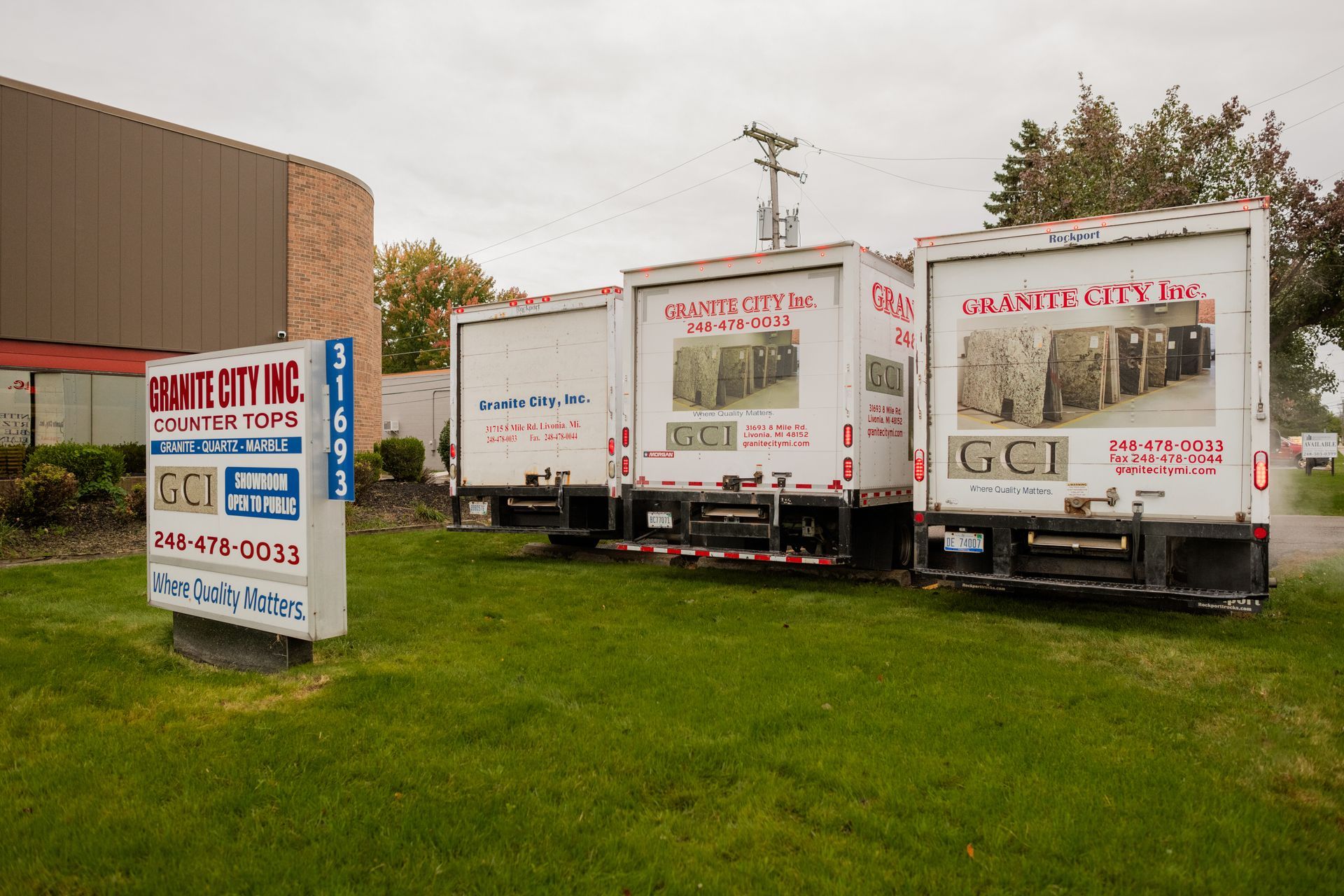 Three white trucks parked on grass beside a building 