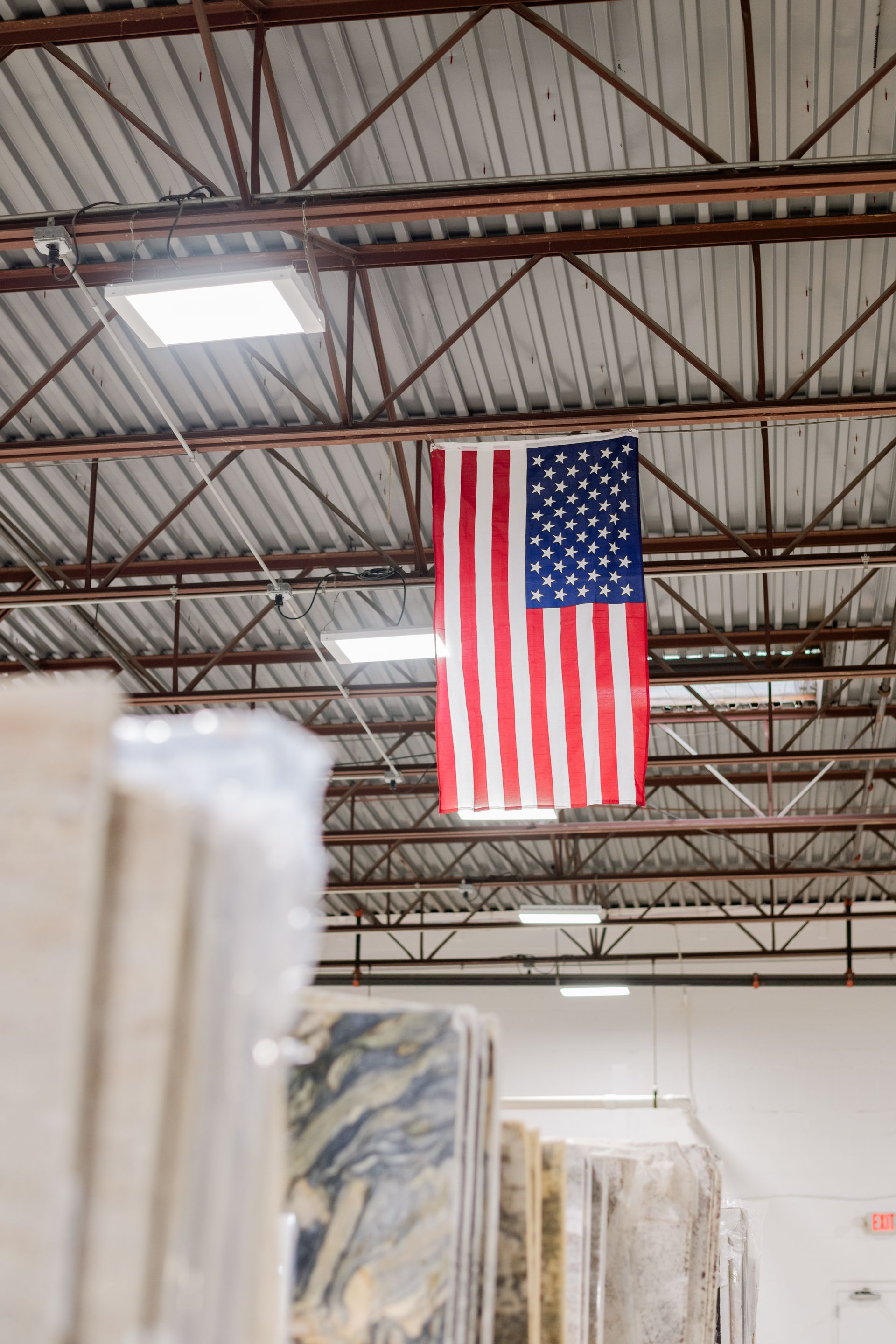 American flag hanging inside an industrial warehouse with high metal beams and racks below