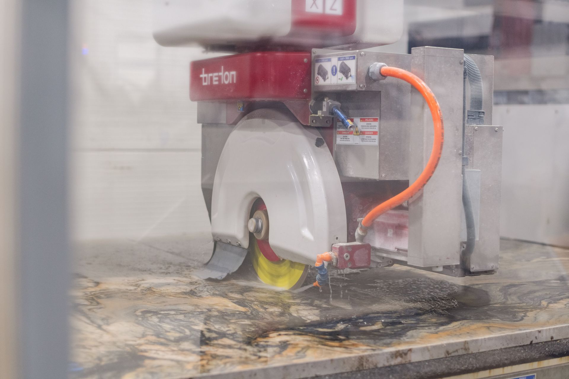 Red industrial saw cutting a stone slab with water spray in a workshop