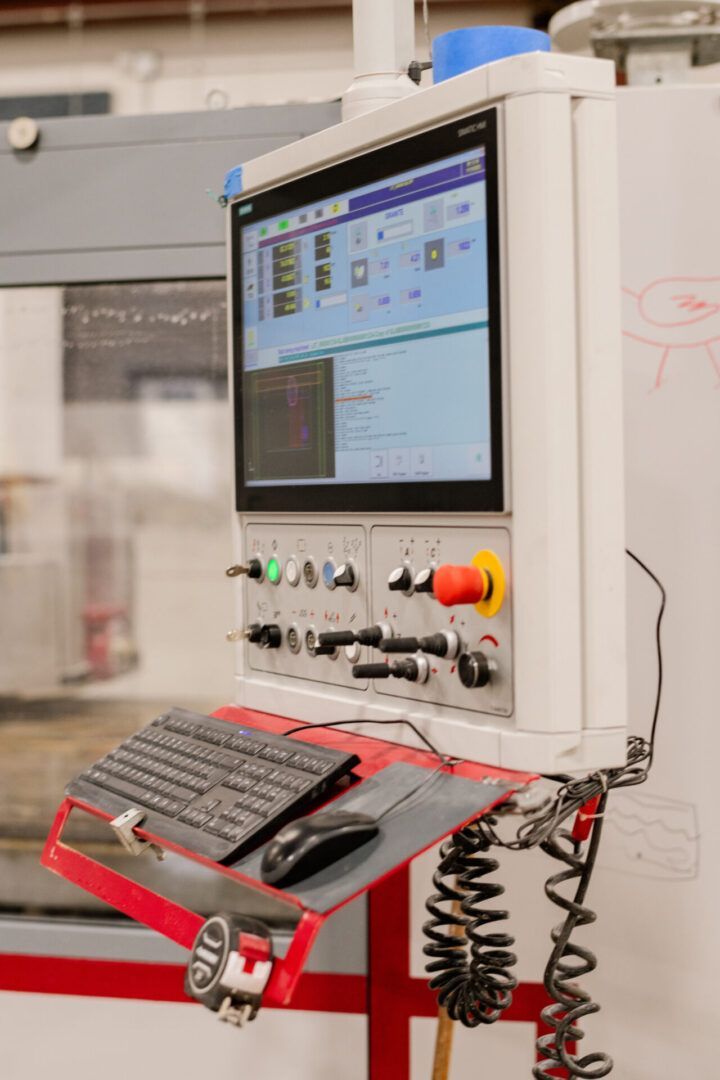 Industrial control panel with monitor, keyboard, and emergency stop button in a factory setting