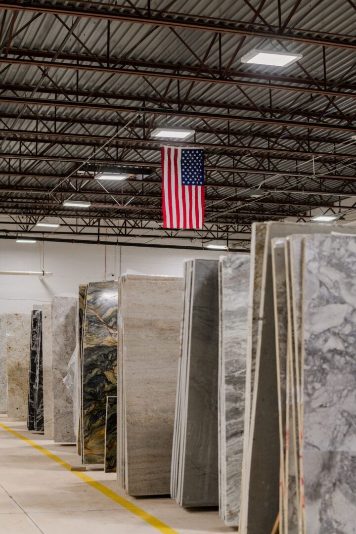 Rows of wrapped stone slabs in a warehouse with an American flag hanging from the ceiling