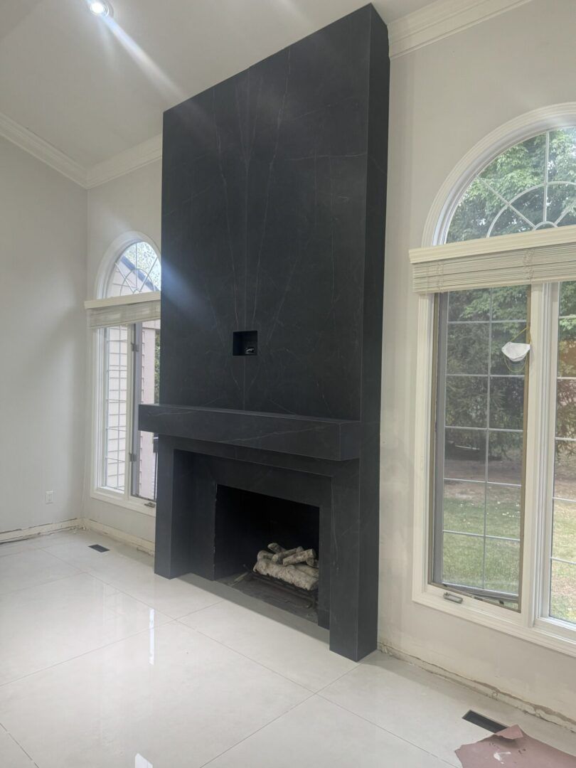 Modern living room with a tall black fireplace wall and large arched windows overlooking a yard.