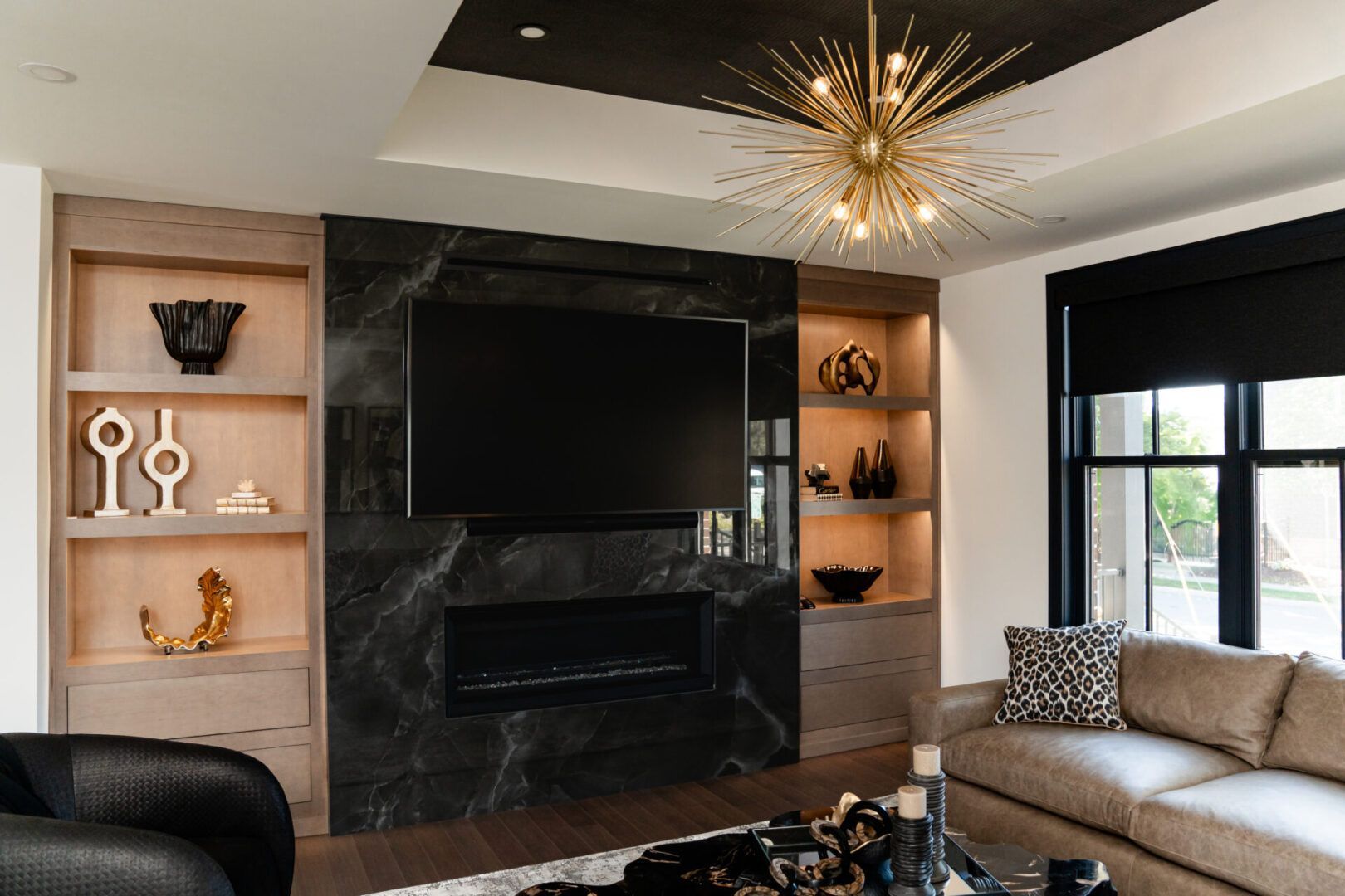 Modern living room with black fireplace, built-in shelves, beige sofa, and starburst chandelier