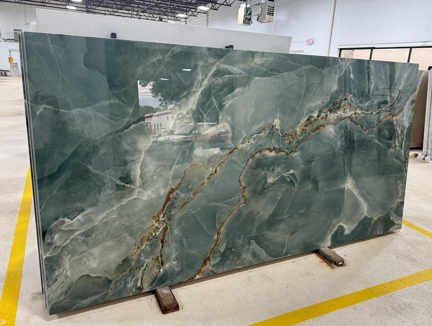 Large green marble slab with white veining displayed upright on metal supports in a warehouse.