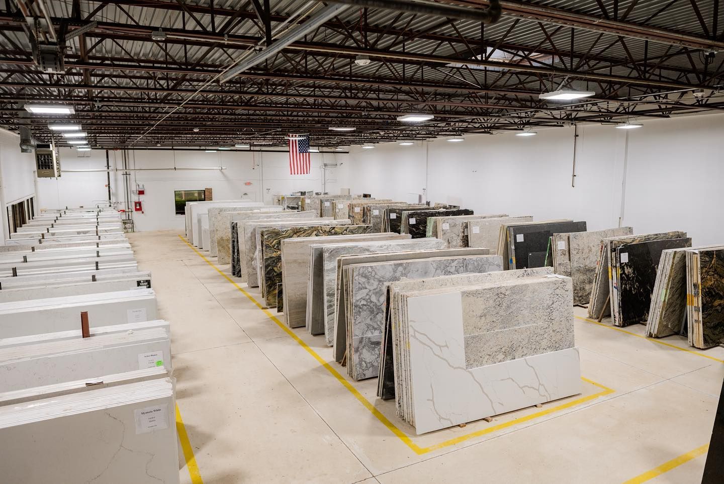 Warehouse interior with rows of large stone slabs and pallets under bright overhead lights