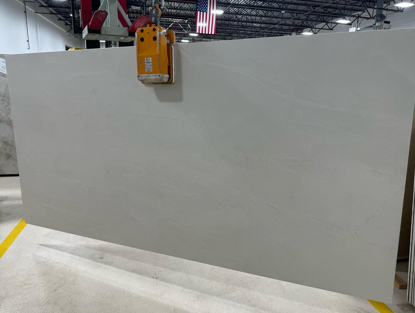 Large white wall panel in an industrial warehouse, with a yellow device mounted near the top.