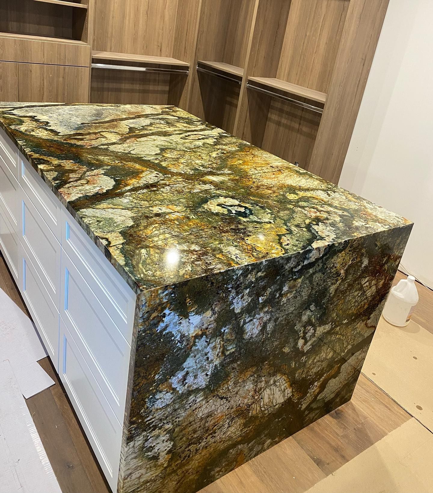 Granite-topped kitchen island with dark green, gold, and black polished stone sides and white drawers