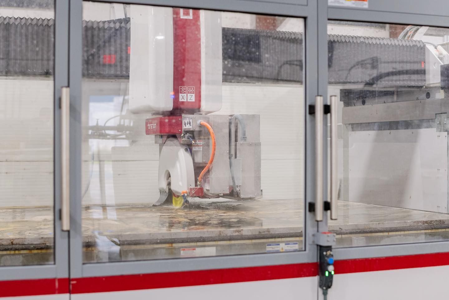Industrial CNC machine behind glass safety panels in a factory.