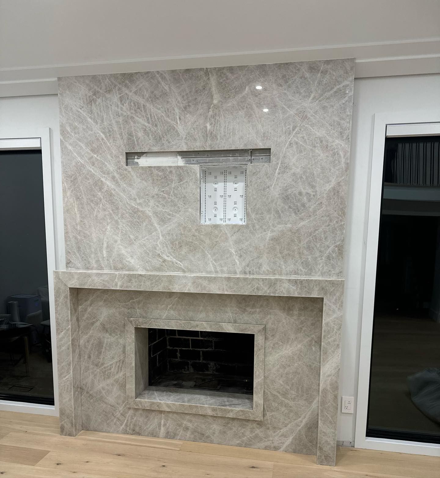 Modern tiled fireplace with a wall-mounted TV bracket and white-framed glass doors on either side
