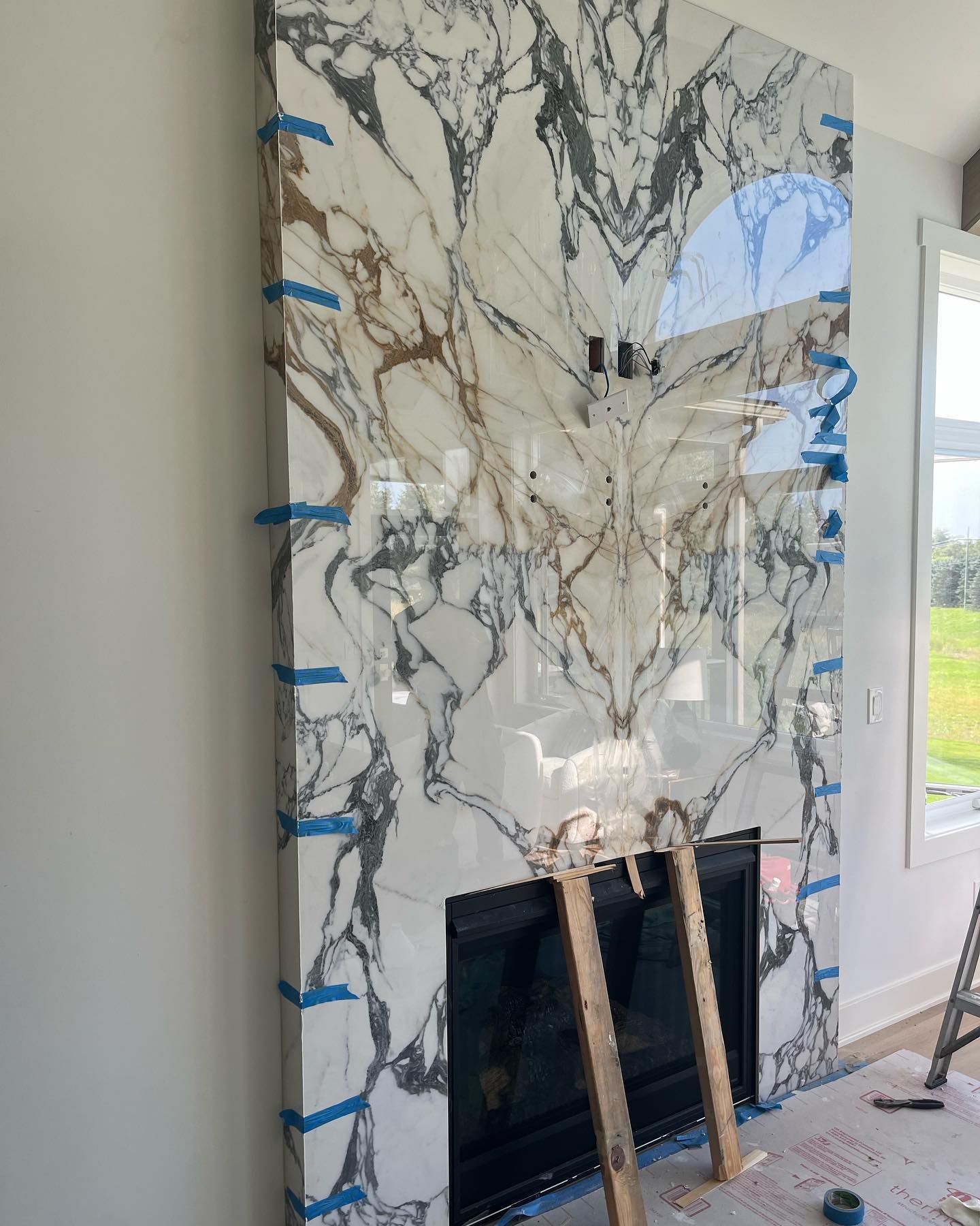 Marble-pattern wall panel being installed above a fireplace opening in a bright room