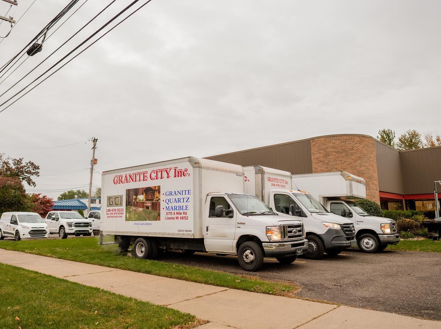 Three white moving trucks parked outside a brick commercial building on a cloudy day