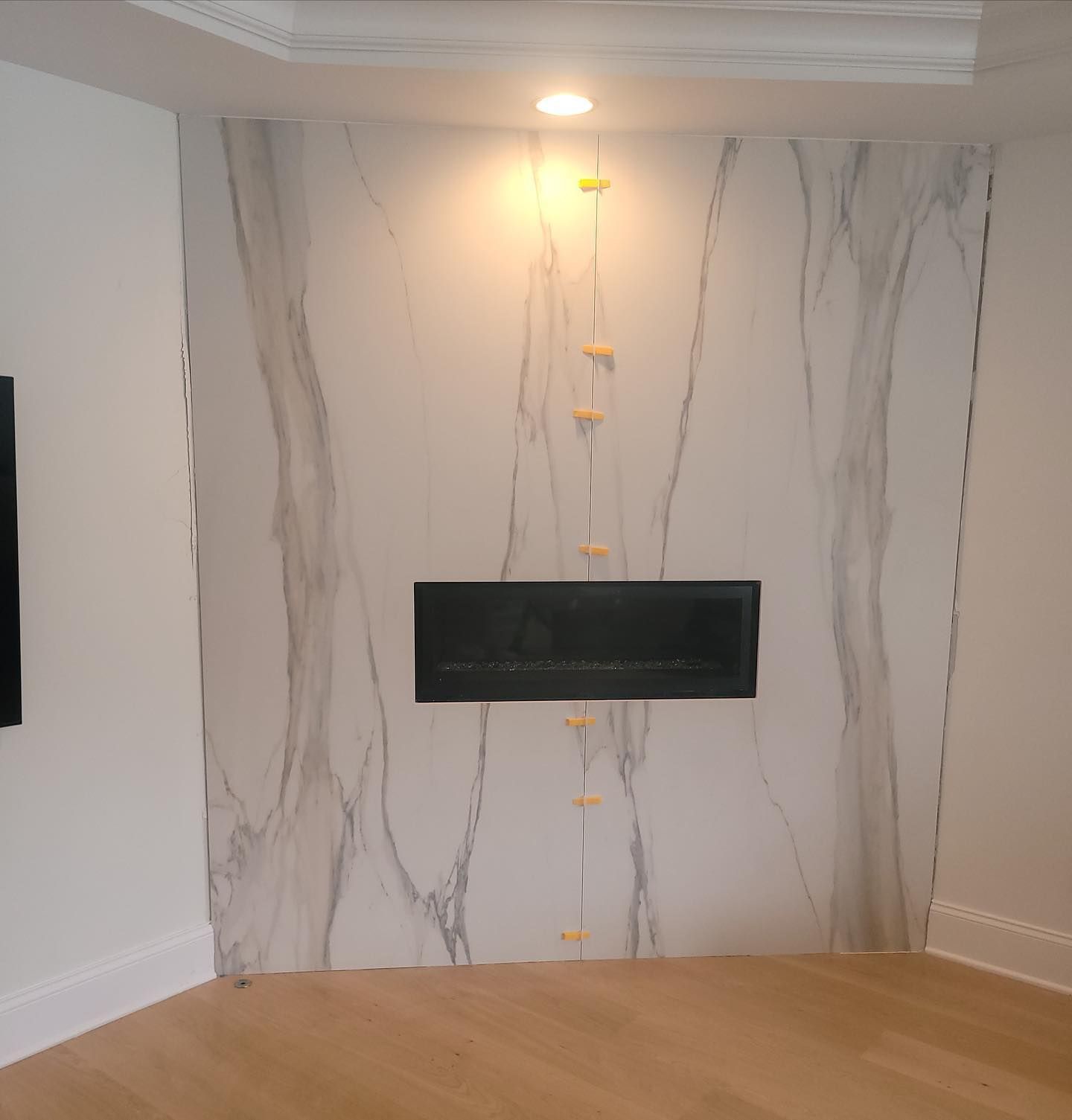 Modern fireplace wall with white marble-look panels, built-in black fireplace, and recessed ceiling light