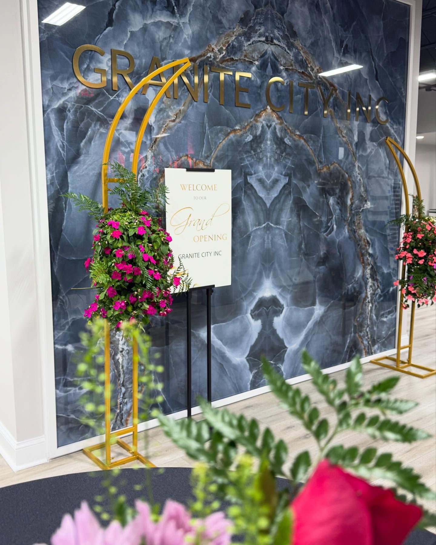 Gold floral entrance sign against blue marble wall with pink flowers and greenery