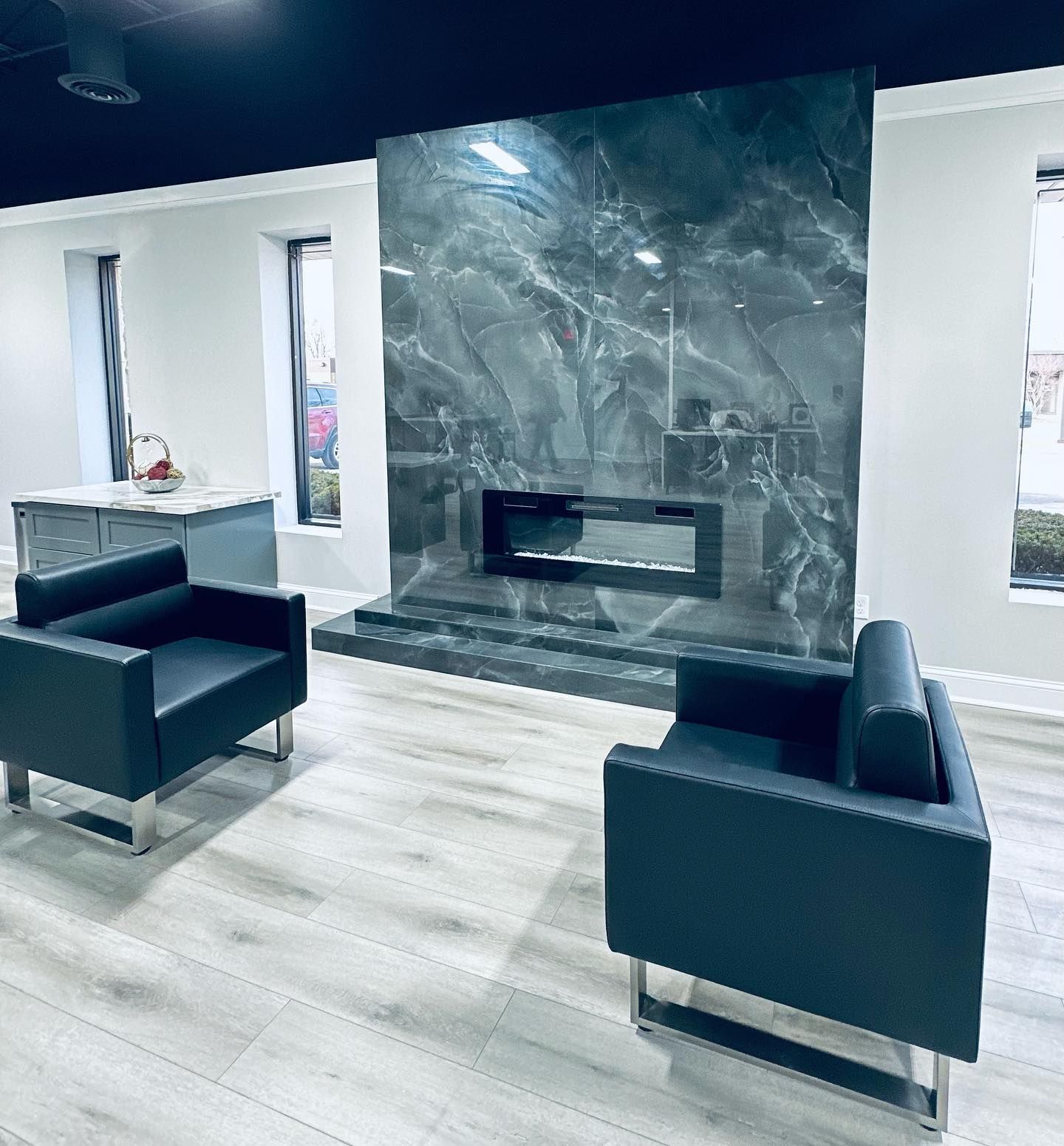 Modern living room with two dark armchairs, light wood floors, and a marble fireplace feature wall.