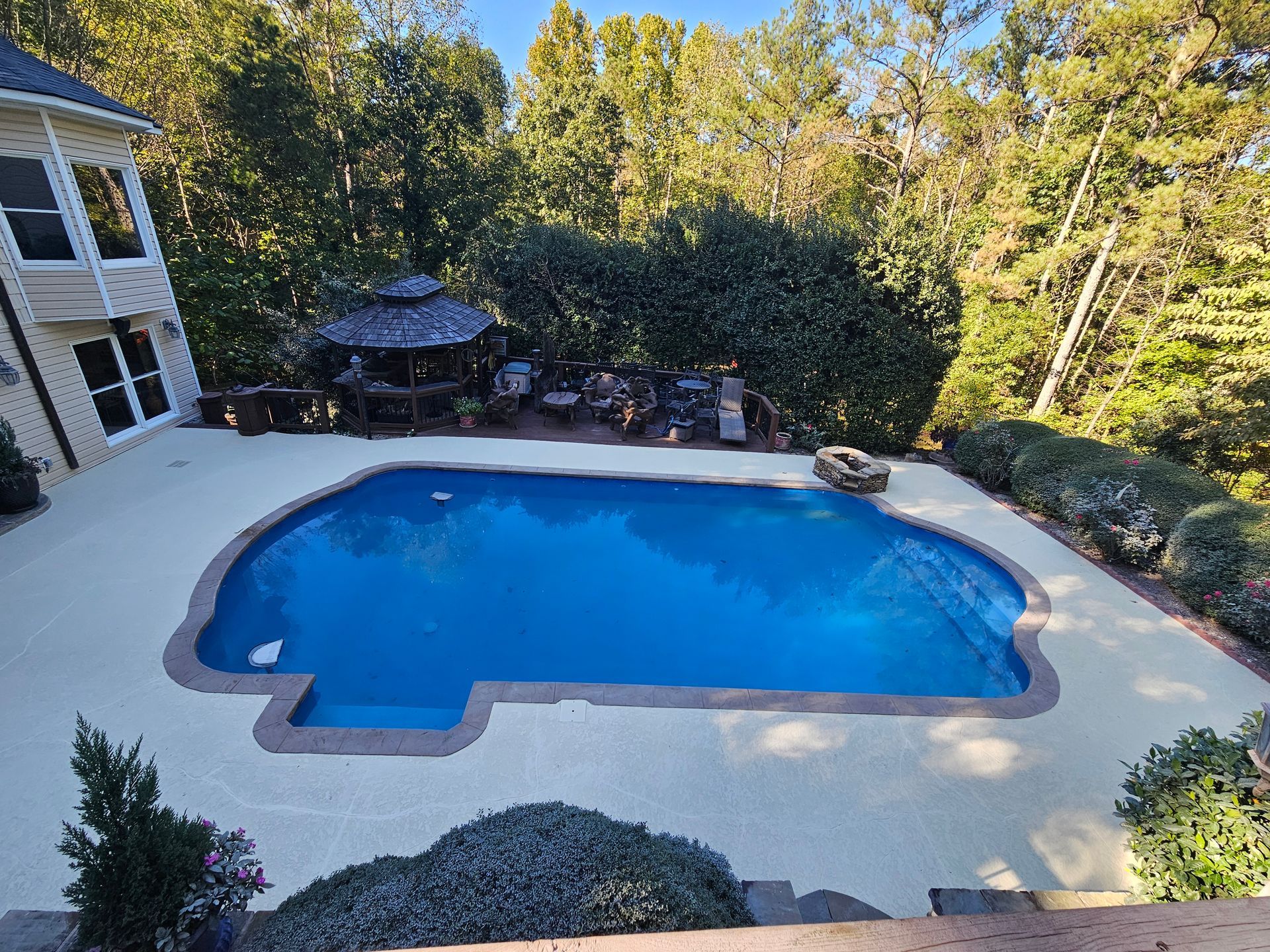A large swimming pool is in the backyard of a house surrounded by trees.