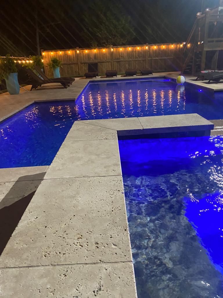 A large swimming pool is lit up at night with blue lights.