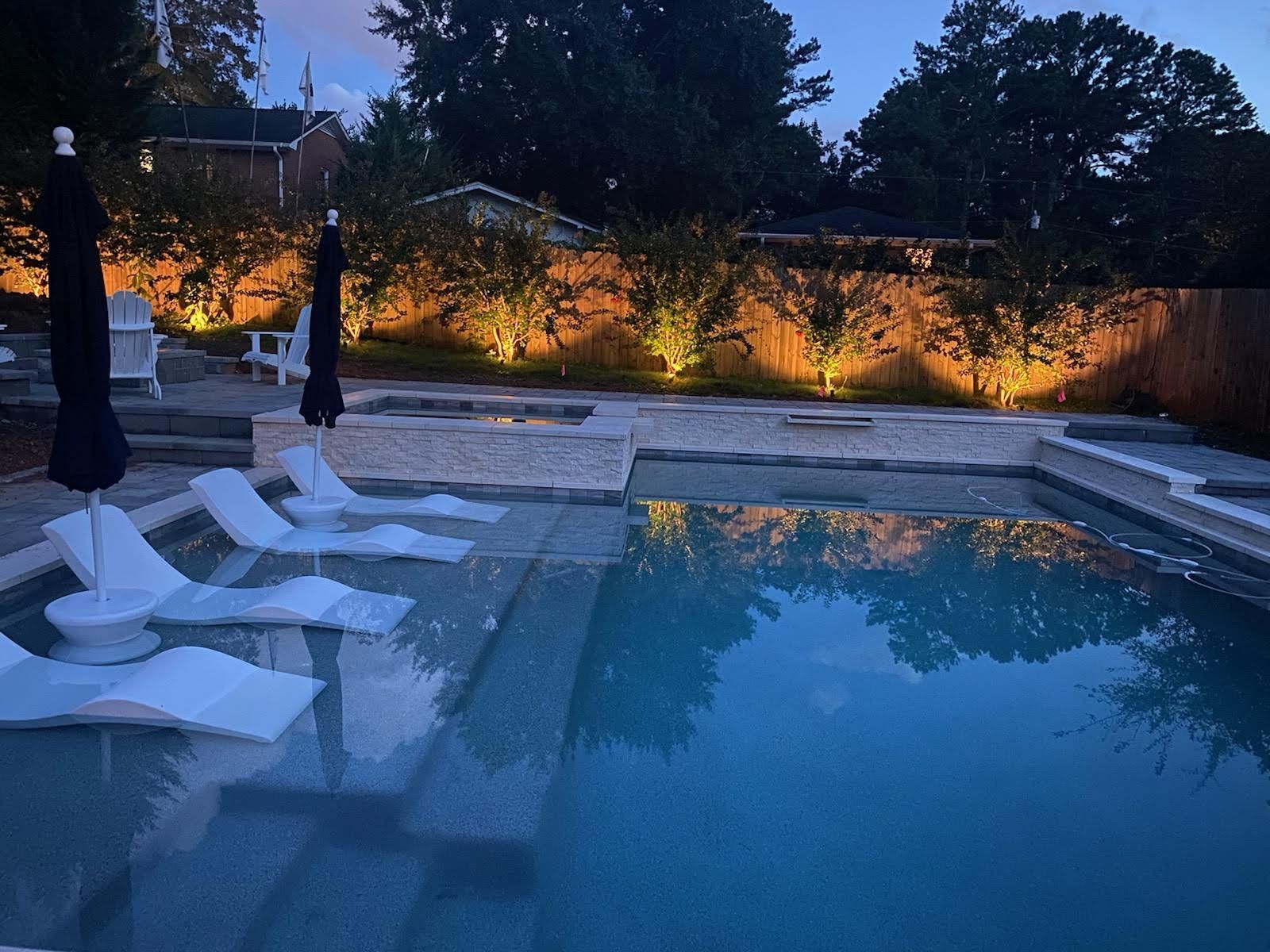 A large swimming pool with chairs and umbrellas around it at night.
