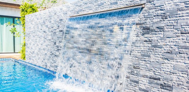 Waterfall cascading into a blue pool, built into a textured stone wall.