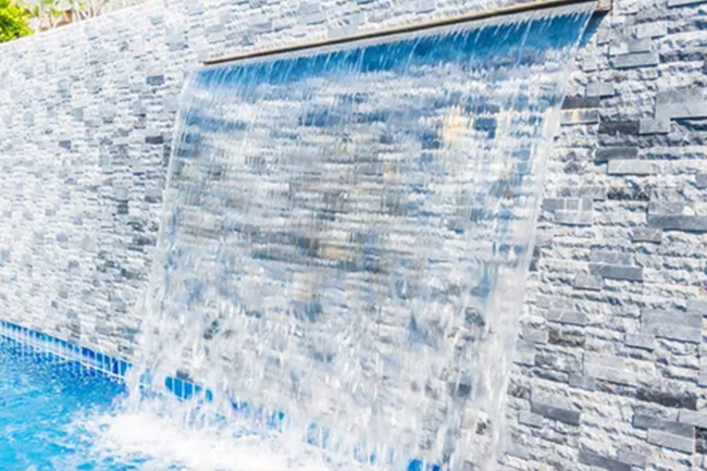 Waterfall cascading into a blue pool, built into a textured stone wall.
