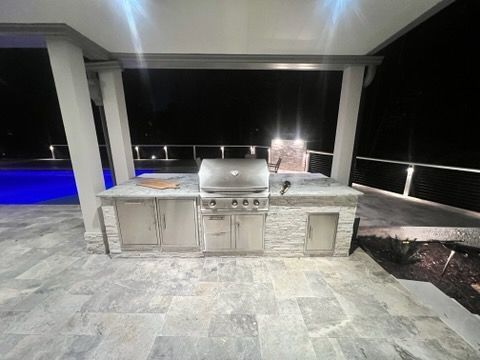 An outdoor kitchen with a grill and a swimming pool in the background.