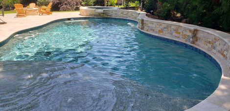 A swimming pool with clear blue water and stone walls, surrounded by trees.