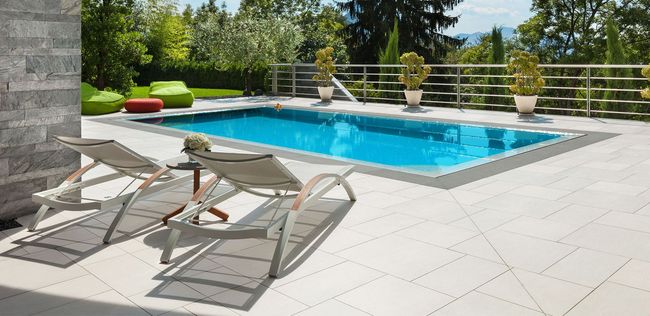 Swimming pool patio with two lounge chairs, side table, pool, and green foliage backdrop.