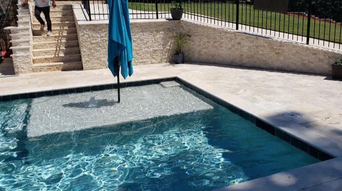 A man is walking down stairs next to a swimming pool with an umbrella.