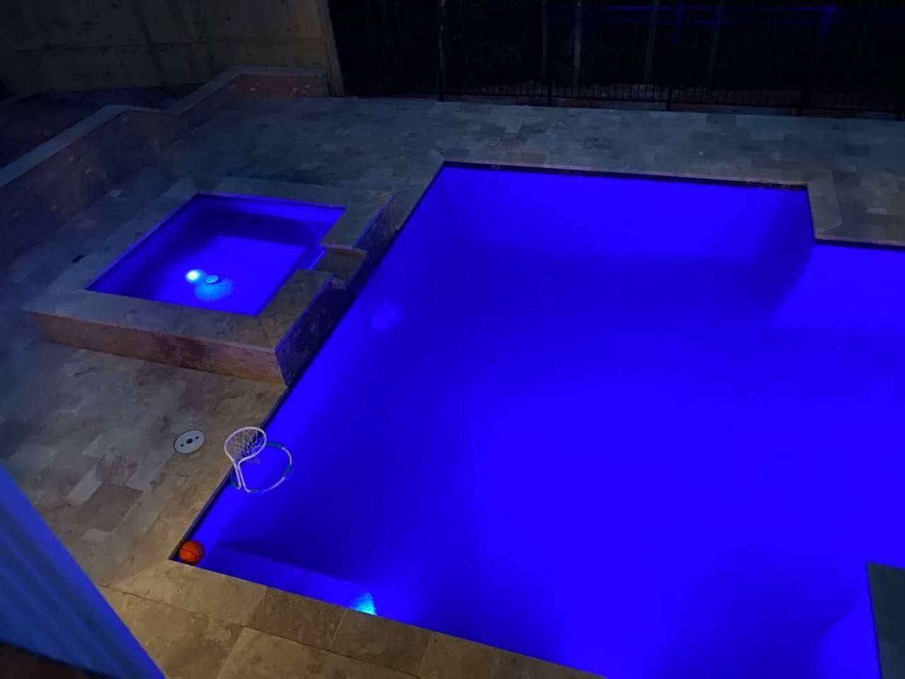 A swimming pool is lit up with blue lights at night