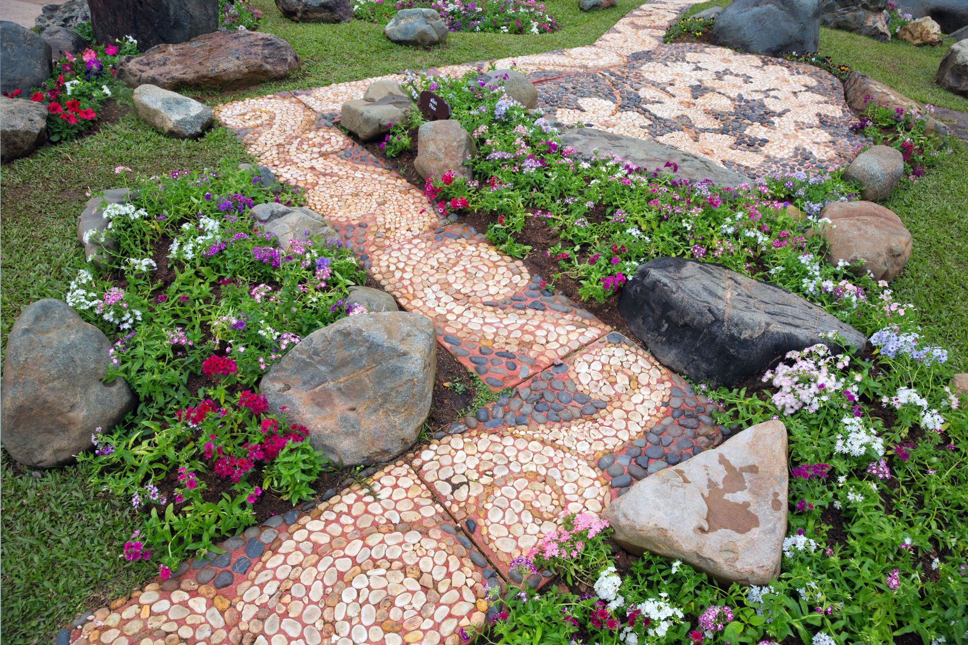 A stone walkway surrounded by flowers and rocks in a garden.