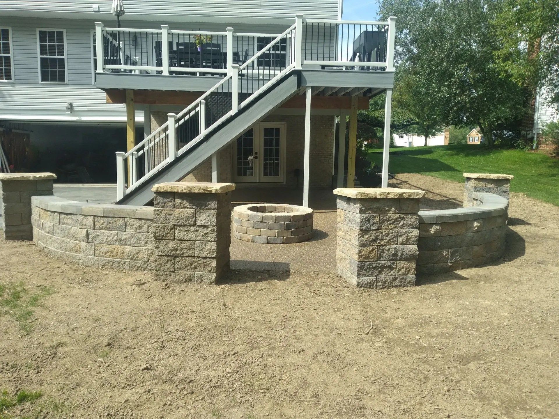 A backyard with a deck, stone fire pit, and seating area on a bed of tan gravel.