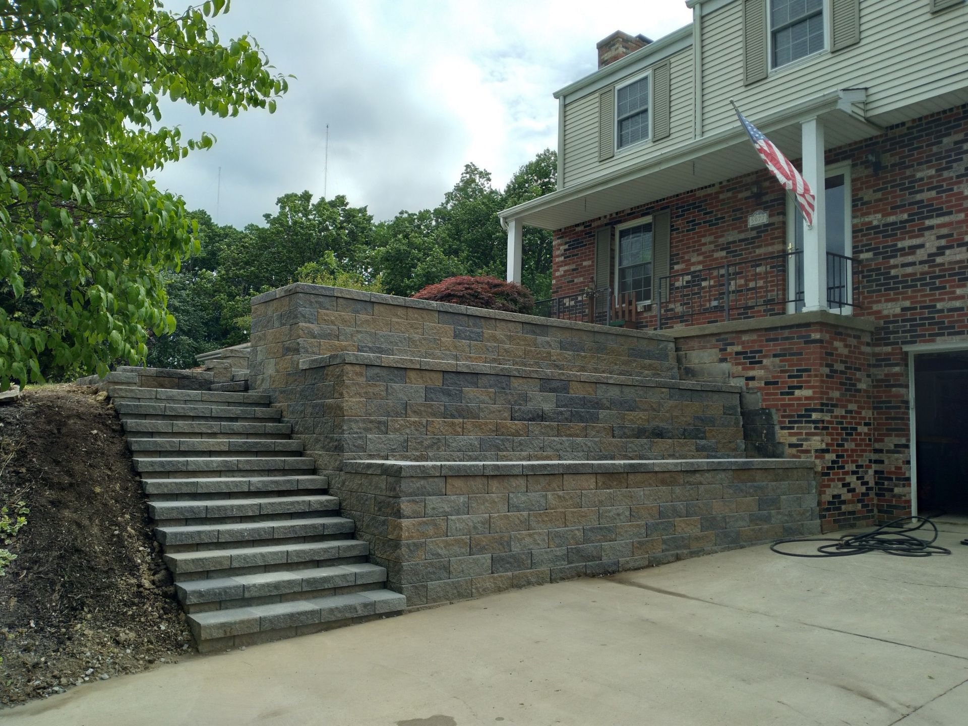 Stone retaining wall and staircase in front of a brick house with an American flag. Dark gray and brown stones are used.