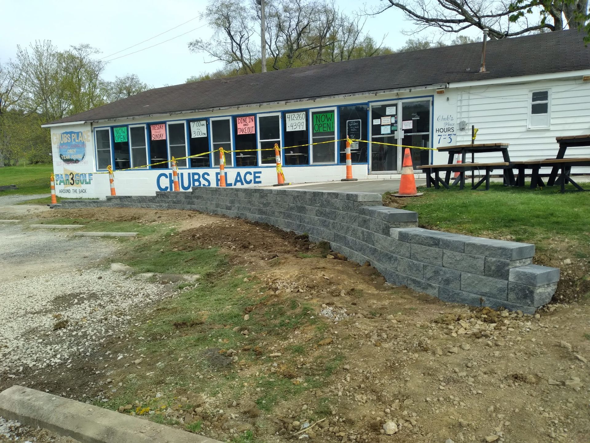 Exterior of Chub's Place, a business with a small retaining wall in front. Construction cones and picnic tables are present.