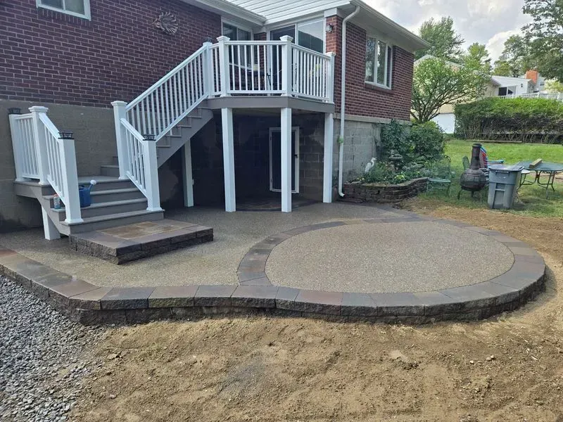 A concrete patio with retaining wall is built adjacent to a house with a sliding glass door.