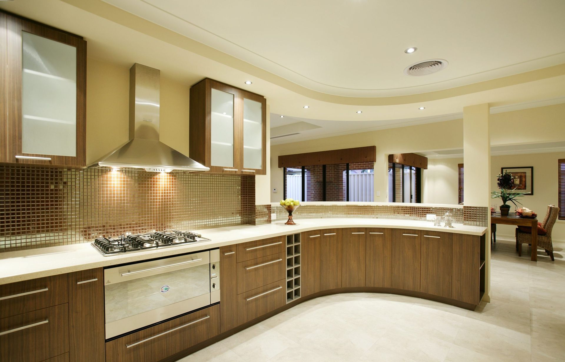 Modern curved kitchen with wood cabinets, stainless appliances, mosaic backsplash, and bright open layout