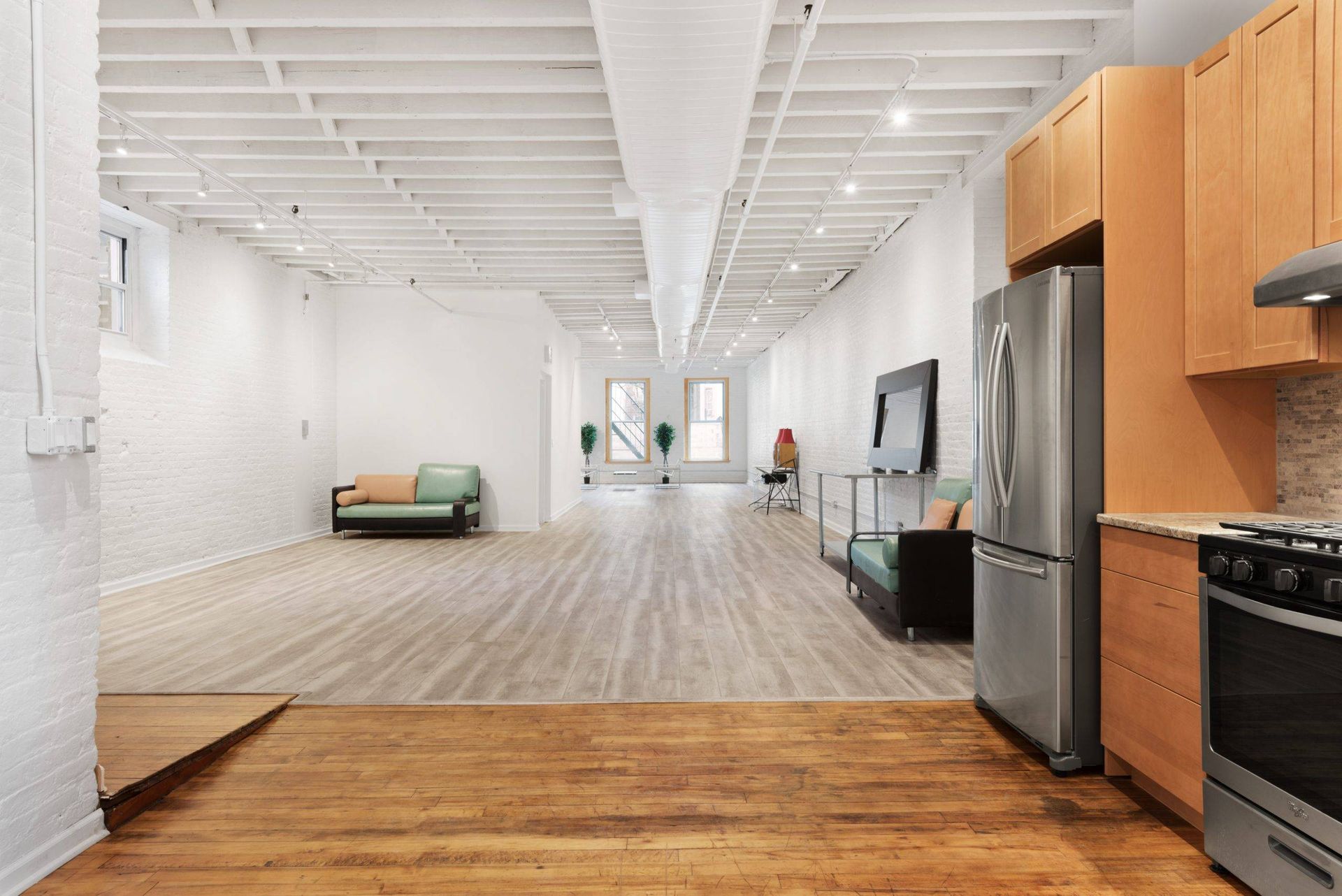 Bright open loft kitchen with stainless steel appliances, wood floors, and a sofa in the distance