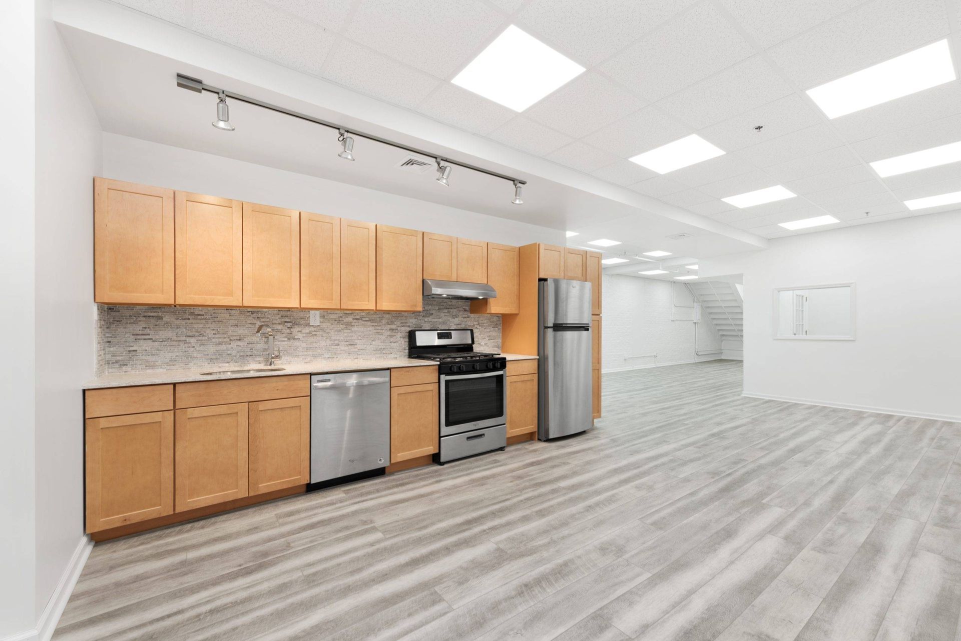 Bright modern kitchen with wood cabinets, stainless appliances, and open gray-floored living area