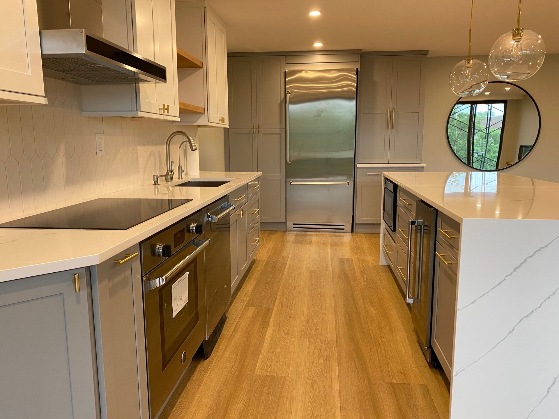 Modern kitchen with white countertops, wood floors, stainless appliances, and a round window at the far end