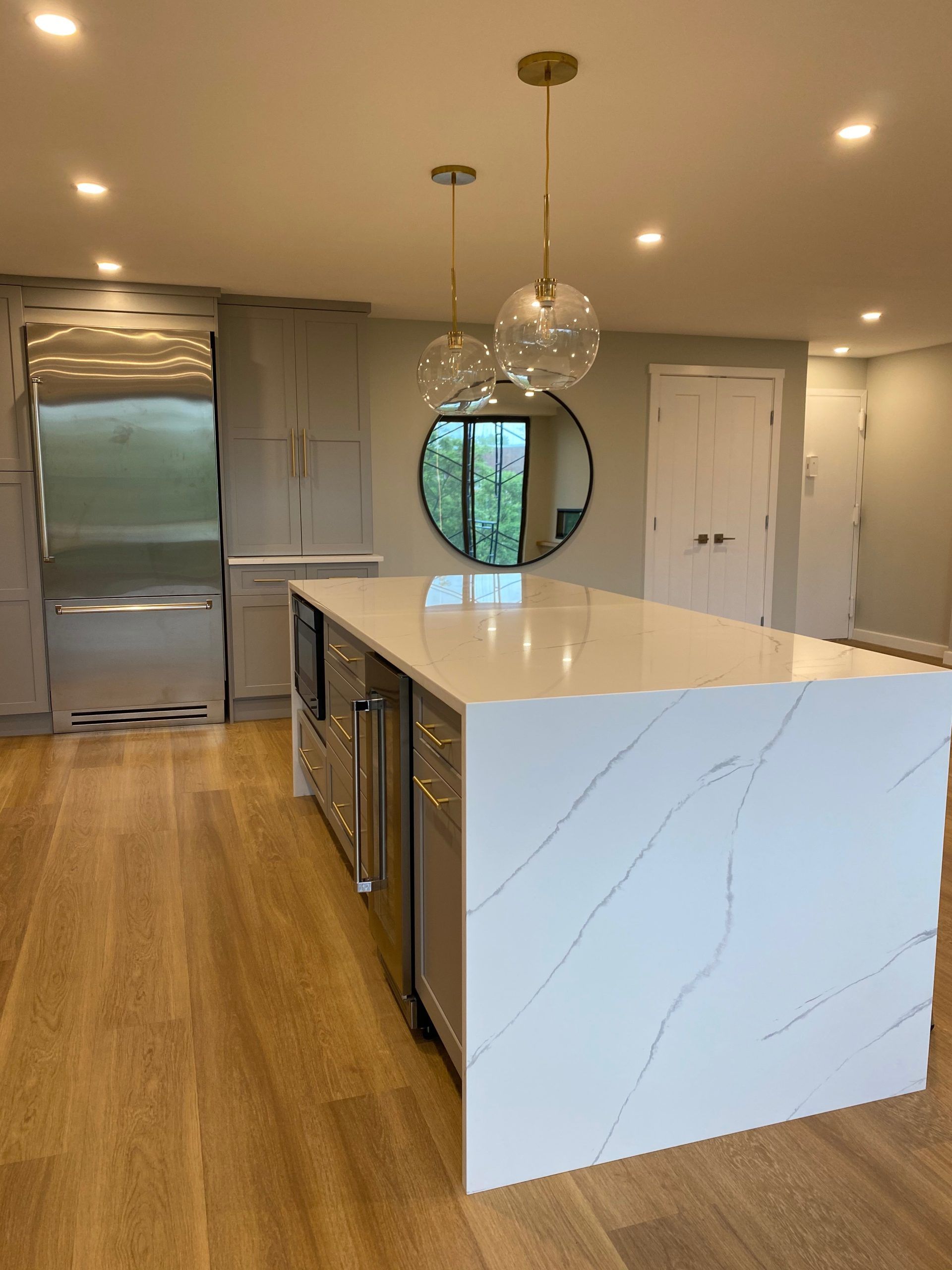 Modern kitchen with large marble island, pendant lights, stainless fridge, and wood floors.