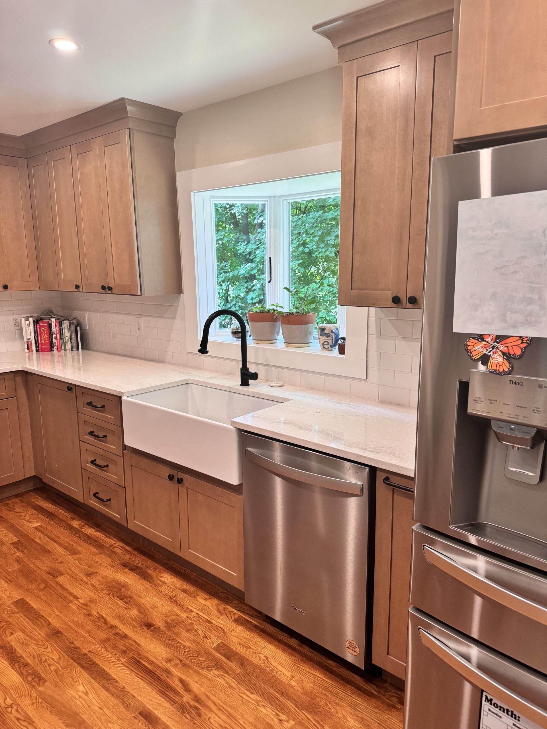 Bright kitchen with wood cabinets, white sink, stainless dishwasher, and refrigerator by a window.