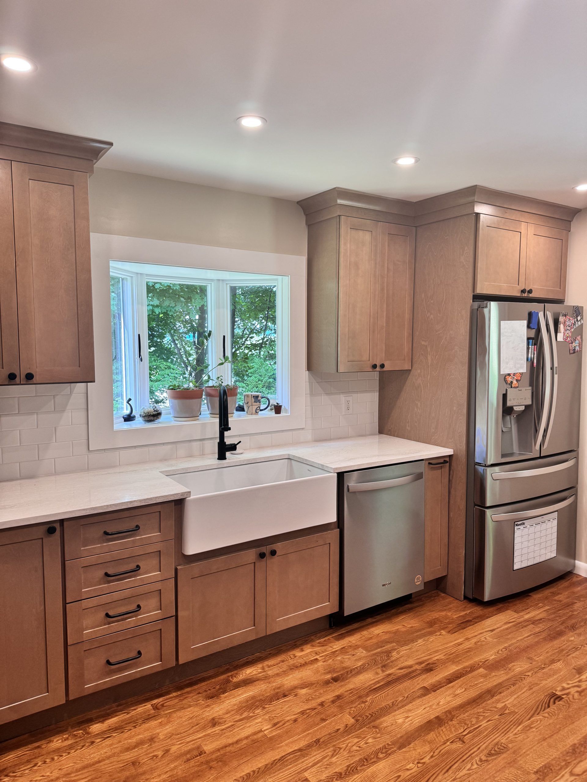 Bright kitchen with wood cabinets, white countertops, farmhouse sink, window, and stainless steel appliances.