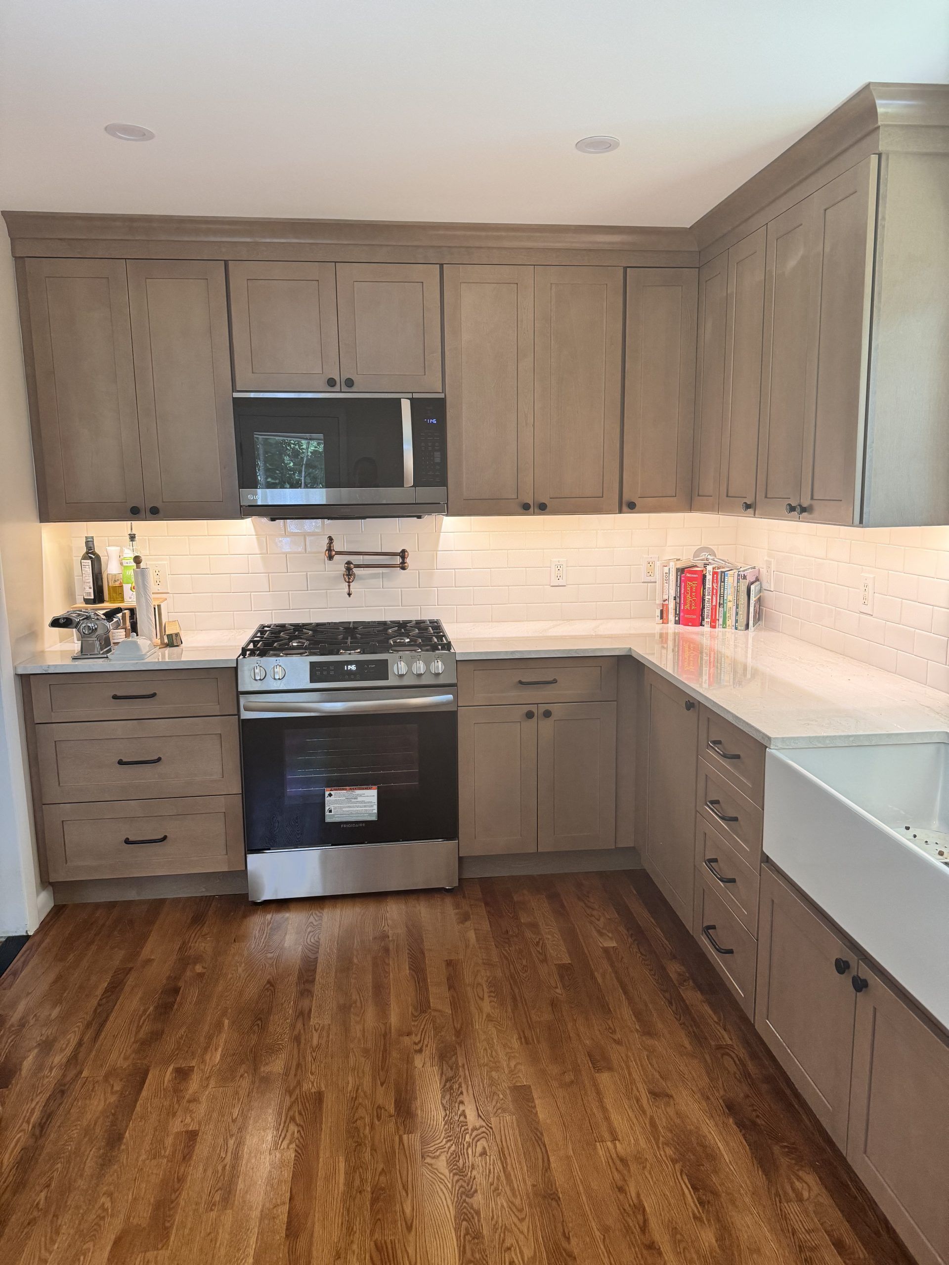 Modern kitchen with gray cabinets, stainless steel stove and microwave, white backsplash, and wood floor
