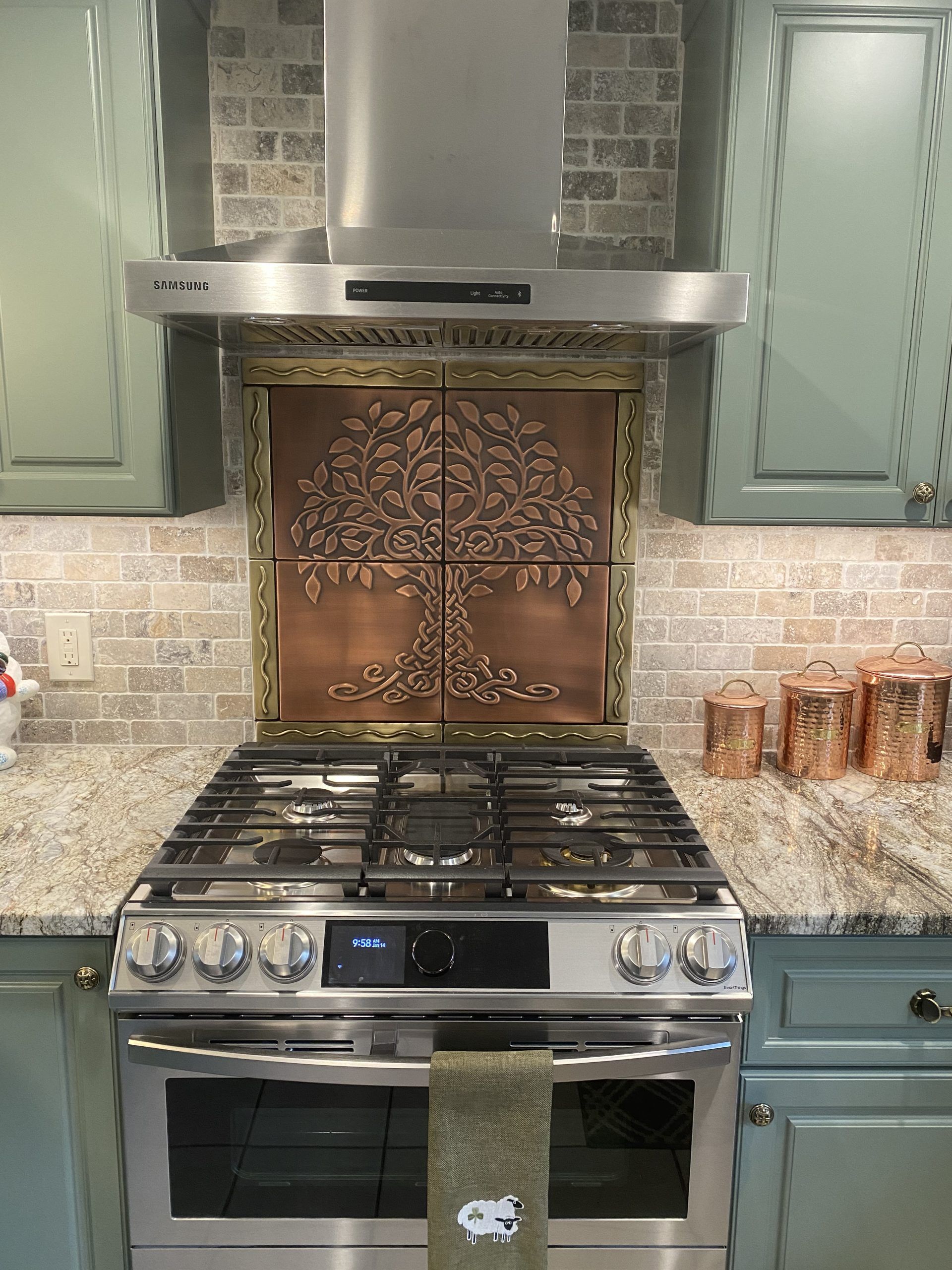 Kitchen stove beneath stainless range hood, with mint cabinets and decorative backsplash tiles.