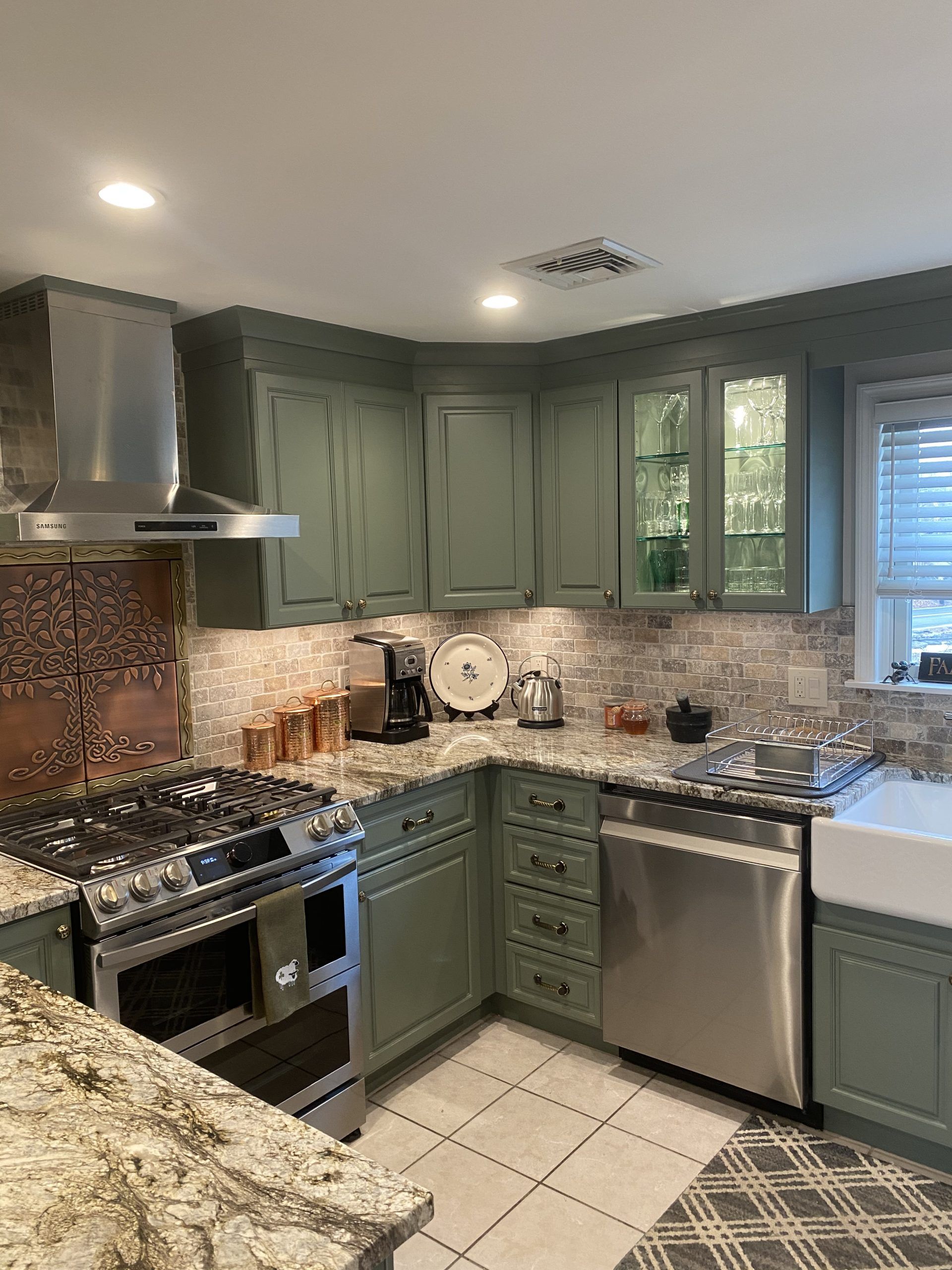 Green kitchen with stainless steel stove, tiled backsplash, and granite countertops.