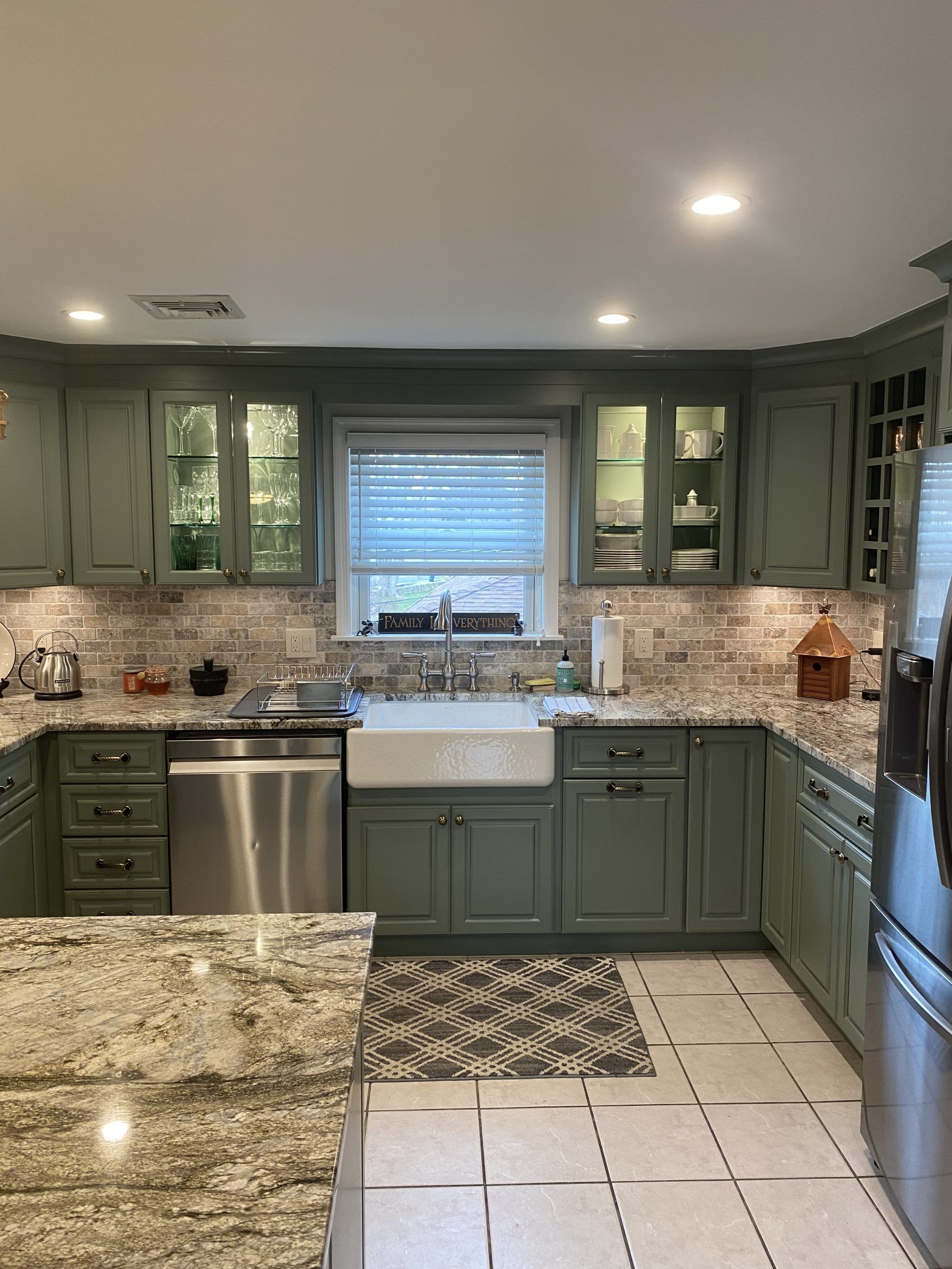 Green kitchen with granite counters, patterned tile floor, and a window above the sink