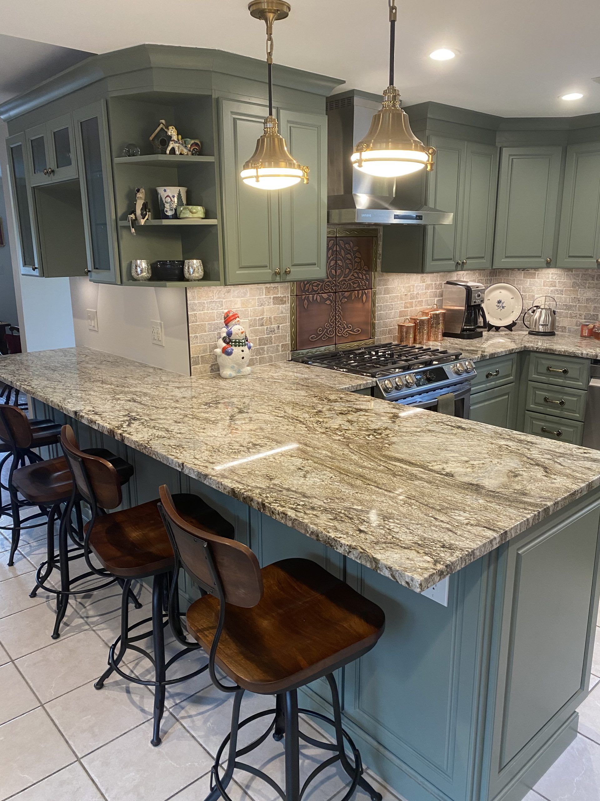 Green kitchen with granite island, pendant lights, bar stools, and stainless steel stove.