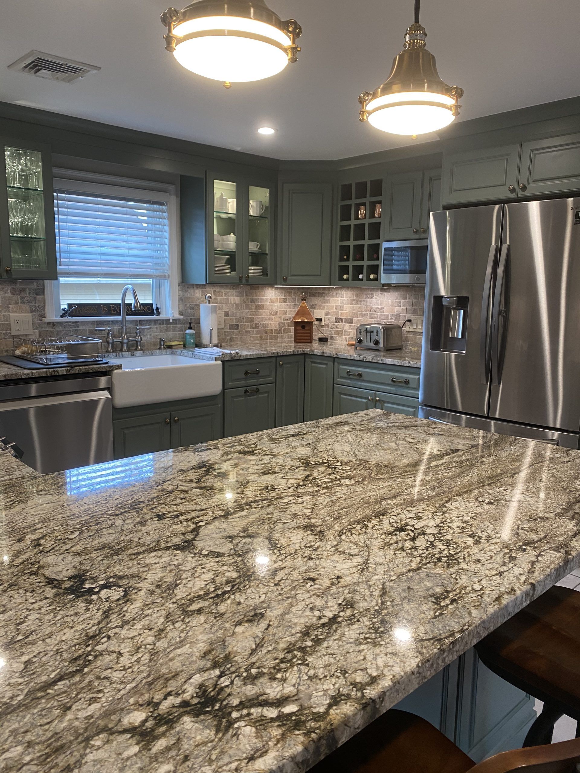 Modern kitchen with granite island, stainless-steel appliances, green cabinets, and pendant lights