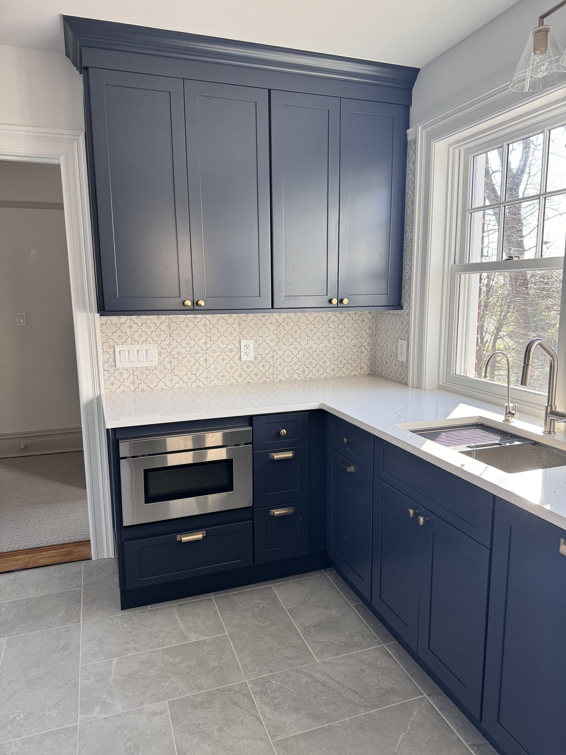 Modern kitchen with navy cabinets, white countertops, patterned backsplash, and a bright window sink area